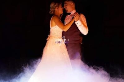 Un couple danse dans une ambiance romantique, entouré de fumée et éclairé par une lumière tamisée.