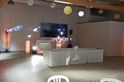 Salle décorée avec des lumières colorées, un écran géant, des tables blanches et des éléments de structure en bois.