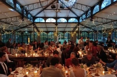 Salle de réception lumineuse avec des invités dînant à des tables décorées de bougies et de guirlandes lumineuses.