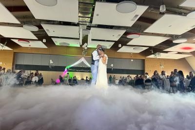 Un couple danse au milieu d'une piste enveloppée de fumée, entouré d'invités dans une salle décorée.