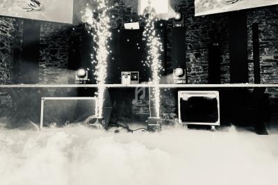 Scène de concert avec effets de fumée et étincelles, entourée de murs en pierre et équipements audio.