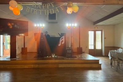 Un DJ anime une fête d'anniversaire dans une salle décorée avec des ballons et une bannière ’Happy Birthday’.