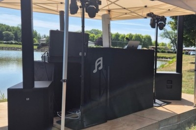 Équipement de sonorisation et éclairage installé sous une tente blanche près d'un plan d'eau.