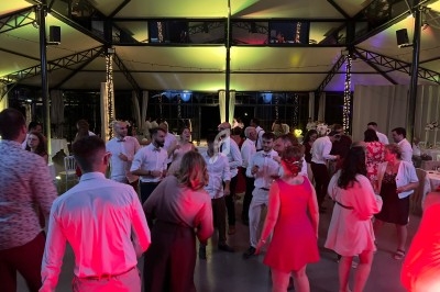 Des personnes dansent dans une salle éclairée de lumières colorées, entourées de tables décorées pour un événement.