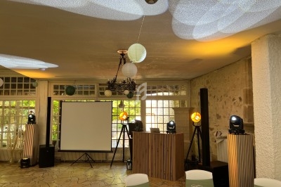 Salle de réception avec projecteurs, écran de projection, tables dressées et décorations lumineuses au plafond.