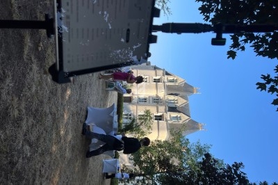 Personnes discutant dans un jardin devant un château, avec un support de tablette visible au premier plan.