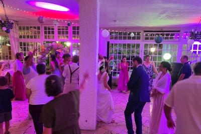 Des invités dansent et discutent dans une salle décorée de lumières colorées et de ballons lors d'une fête.