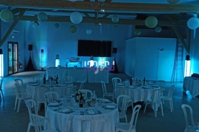 Salle de réception décorée avec des tables rondes dressées, éclairage bleu et lanternes suspendues au plafond.