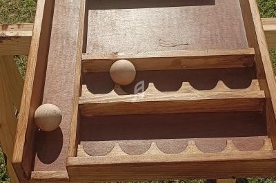 Jeu en bois traditionnel avec des billes en bois sur un plateau incliné, posé sur une structure en extérieur.
