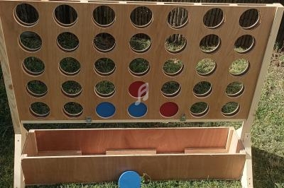 Jeu de puissance 4 en bois avec des jetons rouges et bleus, installé sur une pelouse en extérieur.