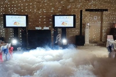 Salle de réception décorée avec des tables dressées, des écrans affichant un menu et un sol recouvert de fumée artificielle.