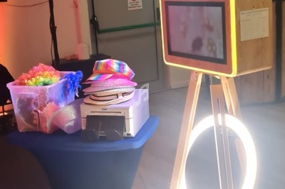 Borne photo interactive sur trépied avec accessoires colorés disposés sur une table dans une salle éclairée.