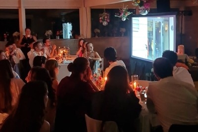 Des invités assis regardent une projection vidéo dans une salle décorée avec des fleurs et des bougies.