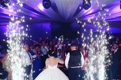 Un couple coupe un gâteau de mariage entouré d'invités sous des jets d'étincelles dans une salle décorée.