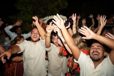 Des personnes souriantes dansent et lèvent les bras lors d'une fête en plein air, de nuit.