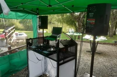 Équipement de DJ sous une tente verte, avec platines, ordinateur portable et enceintes, installé en extérieur près d'un…