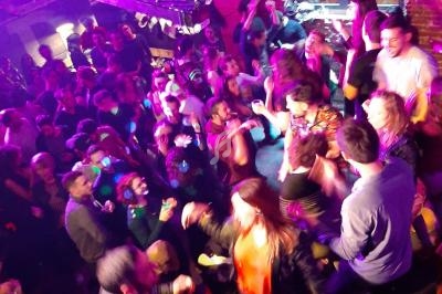 Groupe de personnes dansant et socialisant dans un club animé avec éclairage coloré et ambiance festive.