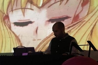 Un homme mixe de la musique sur un équipement DJ devant une projection d'un personnage d'animation.
