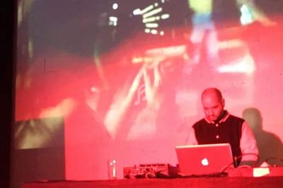 Un homme utilise un ordinateur portable sur une table, avec un fond lumineux et abstrait projeté derrière lui.