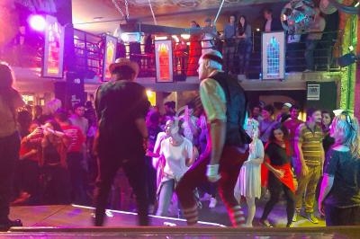 Des personnes dansent sur une scène éclairée devant une foule dans une ambiance festive et colorée.