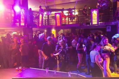 Personnes dansant et socialisant dans une ambiance festive avec éclairage coloré dans un bar ou une discothèque.