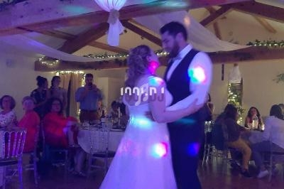 Un couple danse sous des lumières colorées dans une salle décorée pour une réception, entouré d'invités assis.