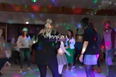 Des personnes dansent dans une salle éclairée par des lumières colorées, créant une ambiance festive.