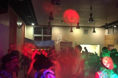 Personnes dansant dans une salle éclairée par des lumières colorées lors d'une fête ou d'un événement festif.