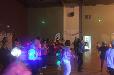 Des personnes dansent dans une salle éclairée par des lumières colorées, lors d'un événement festif en intérieur.