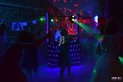 Des personnes dansent dans une salle sombre éclairée par des lumières colorées et un DJ en arrière-plan.