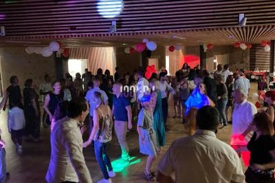 Des personnes dansent dans une salle décorée de ballons rouges et blancs, éclairée par des lumières colorées.