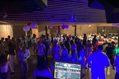 Salle de réception avec des invités dansant et discutant sous des lumières colorées, vue depuis une table de DJ.