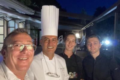 Quatre personnes souriantes, dont un chef en tenue blanche, posent ensemble en extérieur en soirée.