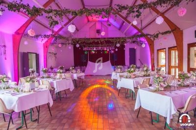 Salle de réception décorée avec des guirlandes végétales, des tables dressées et un éclairage coloré.