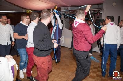 Des hommes participent à une animation festive dans une salle, tenant des rubans colorés sous un éclairage chaleureux.