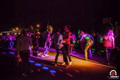 Des personnes dansent sur une piste éclairée par des lumières colorées lors d'un événement nocturne en plein air.