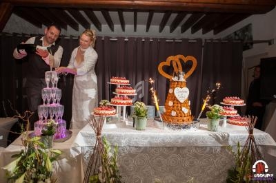 Un couple en tenue de mariage sert du champagne près d'une table décorée avec des desserts et une pièce montée.