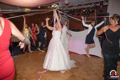 Une mariée en robe blanche joue à un jeu avec des rubans entourée d'invités sur une piste de danse.