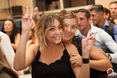Deux femmes souriantes font un signe de paix avec les doigts lors d'un événement festif en intérieur.