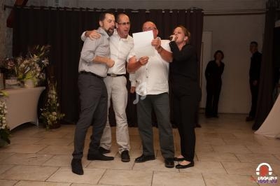 Quatre personnes chantant ensemble devant un public dans une salle décorée avec des fleurs et des rideaux sombres.