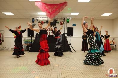 Des danseuses en tenue flamenco exécutent une chorégraphie sur une scène éclairée dans une salle intérieure.