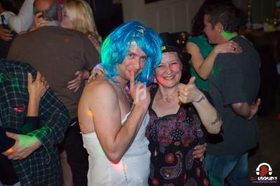 Deux personnes souriantes posent lors d'une fête, l'une portant une perruque bleue et une robe blanche.