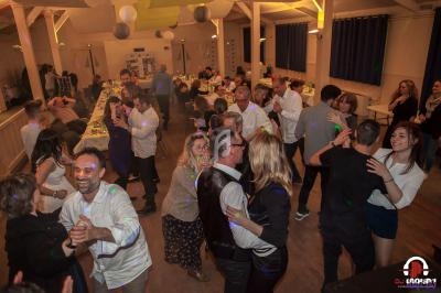 Des personnes dansent et discutent dans une salle de réception décorée, éclairée par des lumières tamisées et colorées.