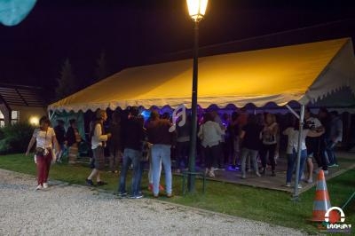 Groupe de personnes rassemblées sous une tente éclairée la nuit, avec une ambiance festive et des lumières colorées.