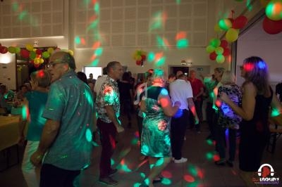Des personnes dansent dans une salle décorée de ballons colorés, éclairée par des lumières de fête.