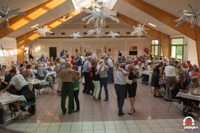 Des personnes dansent et dînent dans une grande salle lumineuse avec une décoration festive au plafond.