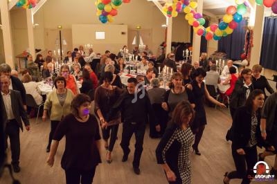 Des personnes dansent en groupe dans une salle décorée de ballons, avec des tables dressées en arrière-plan.