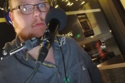 Homme portant un casque audio, parlant dans un microphone dans un environnement faiblement éclairé.