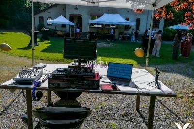 Poste de DJ en plein air sous une tente, avec matériel audio et ordinateurs, lors d'un événement en extérieur.
