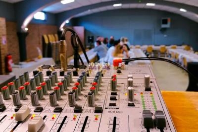 Table de mixage audio en gros plan dans une salle avec des tables et des chaises en arrière-plan flou.
